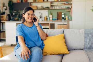Seated comfortably in her stylish living room, a young woman enjoys a phone chat, showcasing emotional engagement and the warmth of domestic life amidst a carefully curated space.