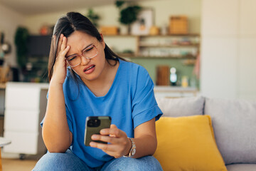 A woman sits on her couch in a cozy home setting, visibly upset as she checks her phone. This image captures the emotional weight of unexpected digital news.