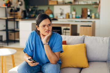 A young woman appears contemplative as she uses her smartphone in a stylish and modern living area, adding a touch of personality to a cozy home environment.