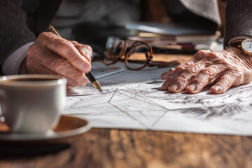 Senior businessman explaining strategy with hand drawn sketches on paper at wooden desk, close up of hands, thoughtful and focused atmosphere, coffee cup and eyeglasses nearby