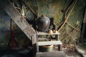 Old wooden staircase corner with traditional jars, gourds, and rustic household items inside an abandoned Chinese house in Papan Heritage Village, Perak, Malaysia
