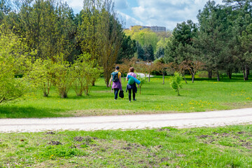 Fototapeta premium Two people enjoy a leisurely stroll through a vibrant green park on a sunny spring day, embracing nature and fresh air. Ideal for recreation, wellness, and outdoor leisure themes.