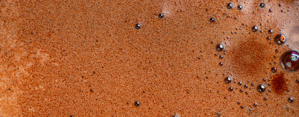 Close-up macro texture of frothy hot chocolate with tiny bubbles and creamy foam surface, showing rich brown color and liquid details for backgrounds, food concepts and beverage design