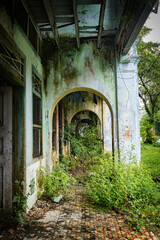 Weathered colonialera corridor in Papan Heritage Village, with peeling paint, overgrown plants, and an old rattan chair adding to the abandoned yet atmospheric charm of this historic Malaysian
