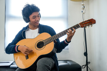 Obraz premium Young Asian Man Wearing Headphones Plays Acoustic Guitar At Home