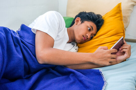 Teenager Relaxing In Bed With Smartphone While Scrolling Social Media With Blanket And Pillows - Powered by Adobe