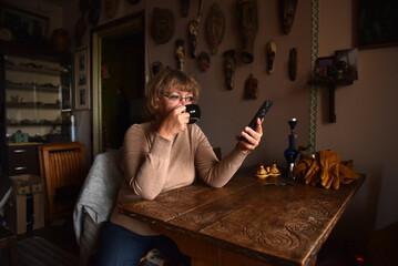 Woman drinking coffee and looking at her smartphone at home