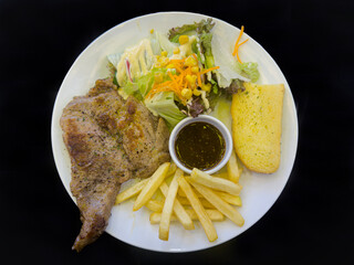 Pork steak served with fries, salad, garlic bread and a sauce in the middle.