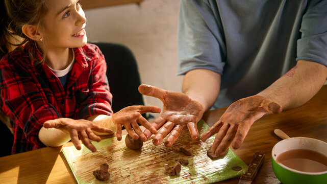 Girl showing muddy clay hands with father during sculpting practice. Concept of hands-on learning, sensory development, creative workshops, and practical family craft skills.