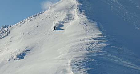 Aerial photo of a free ride skier carving through fresh powder snow on a steep alpine slope. Drone shot capturing the thrill of first tracks in pristine winter mountains.