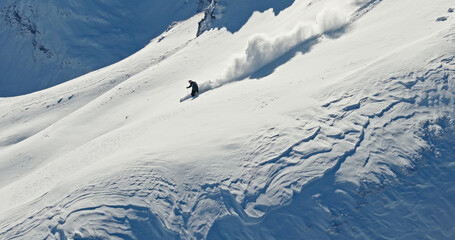 Aerial photo of a free ride skier carving through fresh powder snow on a steep alpine slope. Drone shot capturing the thrill of first tracks in pristine winter mountains.