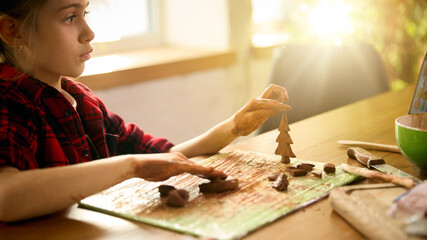 Child shaping small clay tree figure in afternoon craft session. Concept of creative modelling, seasonal DIY projects, early motor-skill training, and practical hands-on learning tasks.