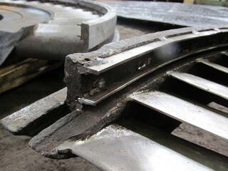 Close-up view of damaged metal component, possibly from turbine or industrial machinery. Jagged edges, evidence of repair work, like welding, are visible on the worn surface. Restoration of diaphragms