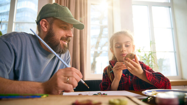 Father and daughter painting small clay figure together near window light. Concept of cooperative crafting, skill-sharing, parent-led learning, practical art activities, and creative family time. - Powered by Adobe
