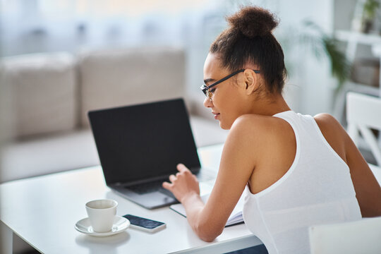 Young woman working at her cozy home office with a cup of coffee by her side