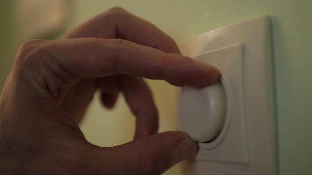 Close-up of a man's hand effortlessly adjusting a wall-mounted dimmer switch to customize the light intensity and conserve energy