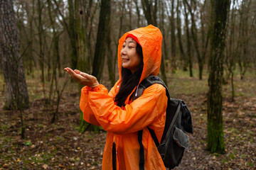 A asian woman spinning around in a orange raincoat in a misty autumn forest, surrounded by wet leaves and nature.