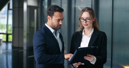 Professional businessman and businesswoman shake hands and smile happily after reviewing documents and successfully closing a deal in a modern corporate office hallway - Powered by Adobe