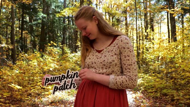 Young Woman in Golden Forest Holds Up words Pumpkin Patch in the Fall with Yellow Leaves 4K Video Stock Footage