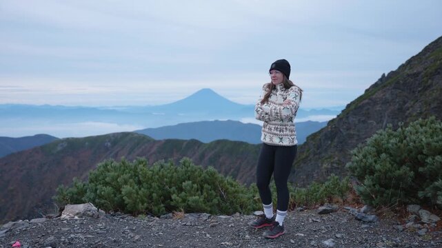 Young caucasian woman in beanie stading on a viewpoint looking at Mt. Fuji from Mt. Kitadake, Japanese Alps.