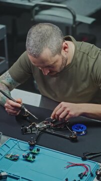 Concentrated Man Using Soldering Iron Secure Microchips and Wiring Onto Drones Central Mainboard. Assembly and Repair of Drones Modern Factory. Technical Detail Modern Drone Assembly. Vertical Shot.