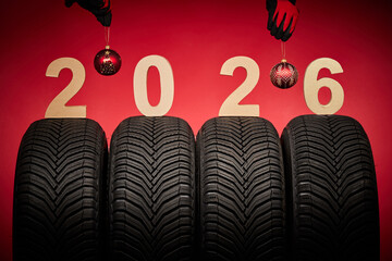 Winter car tires, big wheels service and hands of mechanics with christmas tree ball on new year 2026 red background.