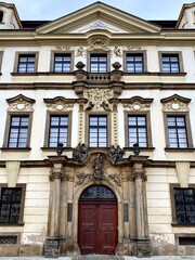Obraz premium Baroque-style building in Hradec Kralove, Czech Republic. Features an elaborate facade with intricate stucco decorations, pilasters, and ornamental sculptures above the entrance.