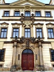 Fototapeta premium Baroque-style building in Hradec Kralove, Czech Republic. Features an elaborate facade with intricate stucco decorations, pilasters, and ornamental sculptures above the entrance.