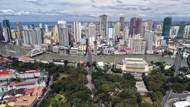 High angle drone view from Intramuros looking toward Binondo, the Chinatown district of Manila, Philippines. The scene shows a dense mix of colorful high-rise buildings along the Pasig River, bridges