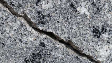 Textured close-up of a grey stone surface with a deep, rugged crack, emphasizing the natural imperfections and coarse grain of the material, perfect for backgrounds