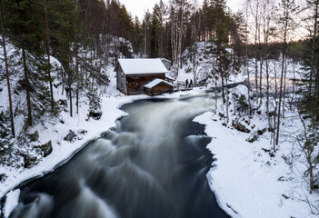 winter river flowing by old wooden mill in snowy finnish forest in National park Oulanka