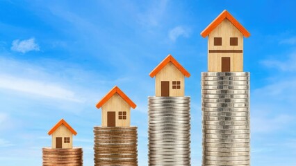 Four wooden houses on stacks of coins against a blue sky showing property value appreciation concept