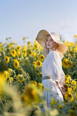Beautiful blonde girl in a white dress in a field of sunflowers