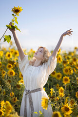 Beautiful blonde girl in a white dress in a field of sunflowers