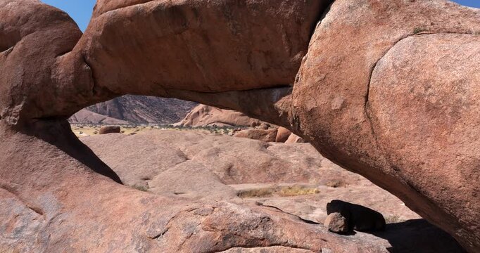 Aerial drone shot flying backward through the iconic rock arch at Spitzkoppe in the Namib Desert, Namibia.
