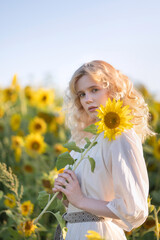 Beautiful blonde girl in a white dress in a field of sunflowers