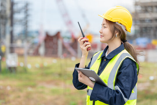 Medium shot of an Asian female engineer overseeing a complex project at an industrial port, overseeing shipping activities and coordinating with multiple teams to maintain steady progress.