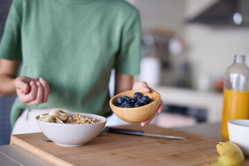 Portrait of a young woman preparing and eating breakfast, drinking juice in the kitchen at home