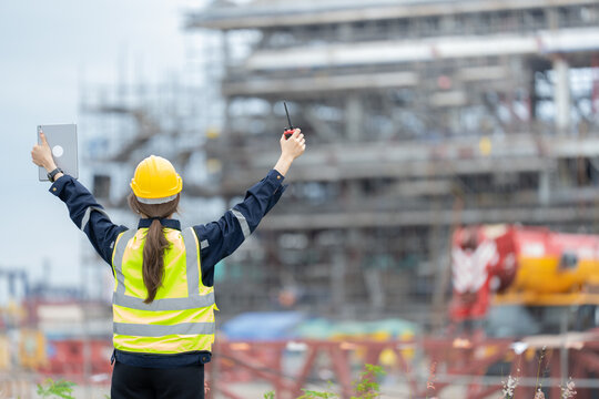 A female supervisor stands at an industrial dock, checking shipping reports and adjusting workflow strategies to improve project accuracy and consistency, using a laptop and a walkie-talkie. - Powered by Adobe