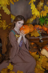 Long-haired girl in a studio among leaves and pumpkins