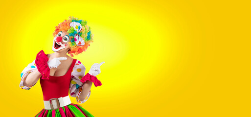 Funny female clown pointing at blank template copy spase for advertising, posters, greetings, invitations. Entertainer as Joker in a suit and wig, with clown whiteface makeup