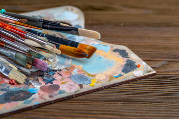 Fototapeta premium Old used brushes in an artist's studio, palette with multi-colored spots of oil or acrylic paint