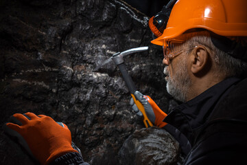 A man in a hard hat with a flashlight examines rock using a pickaxe. Geology, speleology, mining...