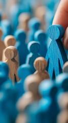 Fototapeta premium Hand selecting a blue wooden figure from a crowd of smaller figures symbolizes leadership and decision-making amidst a diverse group, ideal for business concepts and teamwork themes.