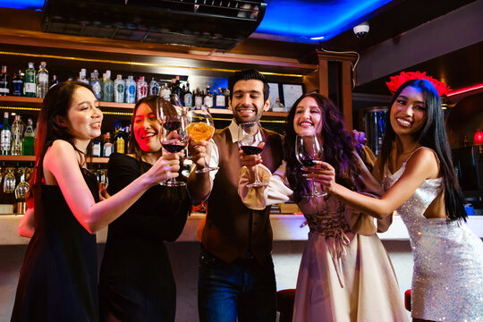 A group of friends celebrates at a lively bar, raising their glasses in a joyful toast amid bottles, laughter, and festive lights—capturing the spirit of nightlife and shared memories.