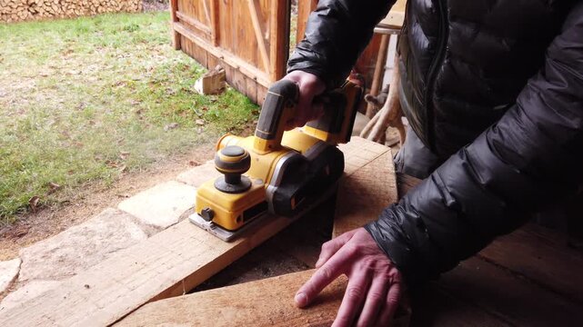 Hands of carpenter working with cordless brushless planer smoothing wooden board