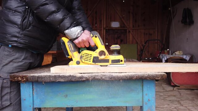 Hands of carpenter working with cordless brushless planer smoothing wooden board