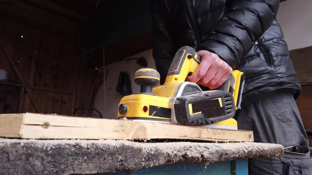 Hands of carpenter working with cordless brushless planer smoothing wooden board