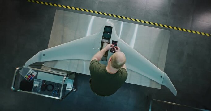 Worker Assembling Drones For National Security. Adult Man in Camouflage Engaged in Specialized Assembly of Large, High tech Drone on Metal Workbench. Future of National Security Production. Top View.