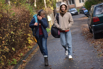Obraz premium Mother and younf adult daughter walking on a street in autumn with backpacks and headphones